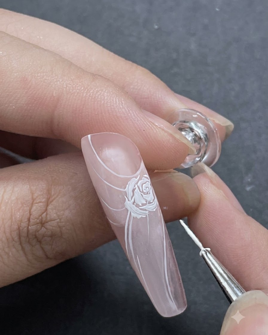A close-up shot showing fine white petal accents being added around the main rose design with a liner brush.