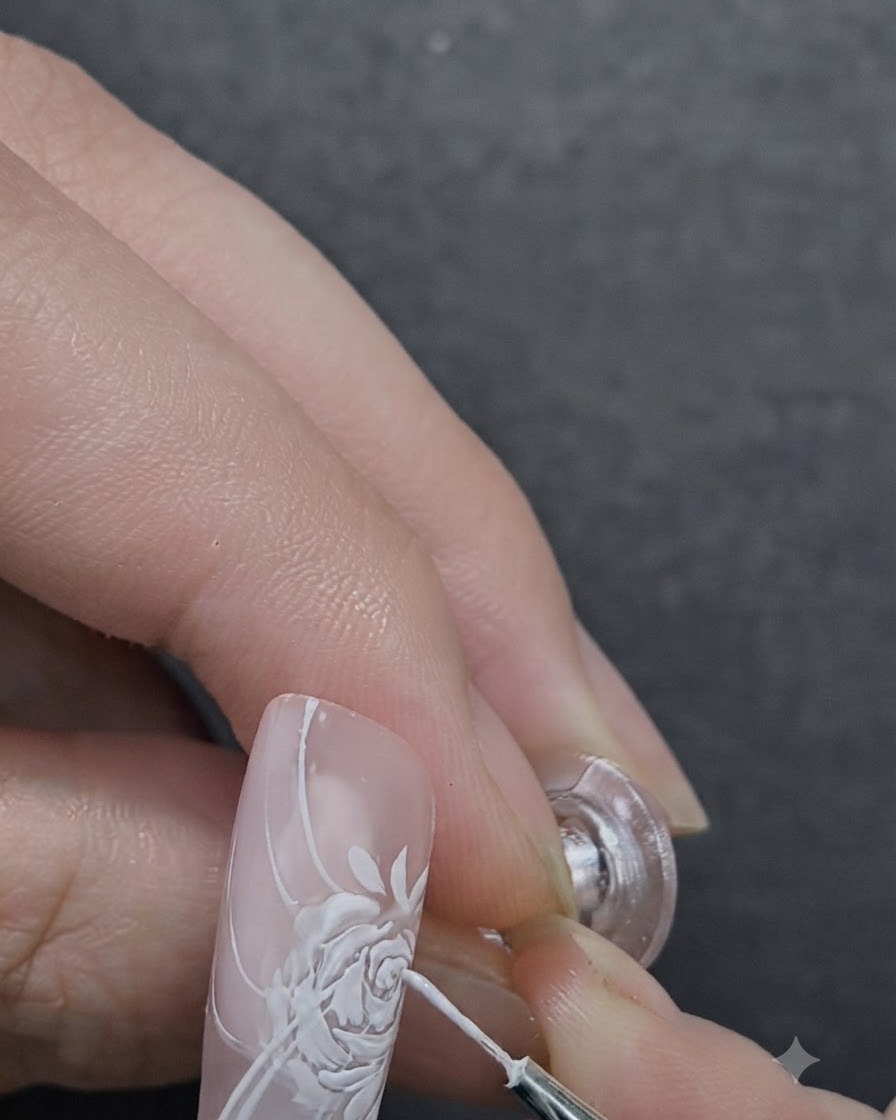 A nail artist applying 3D sculpting gel to the center of a painted rose using a detail brush.