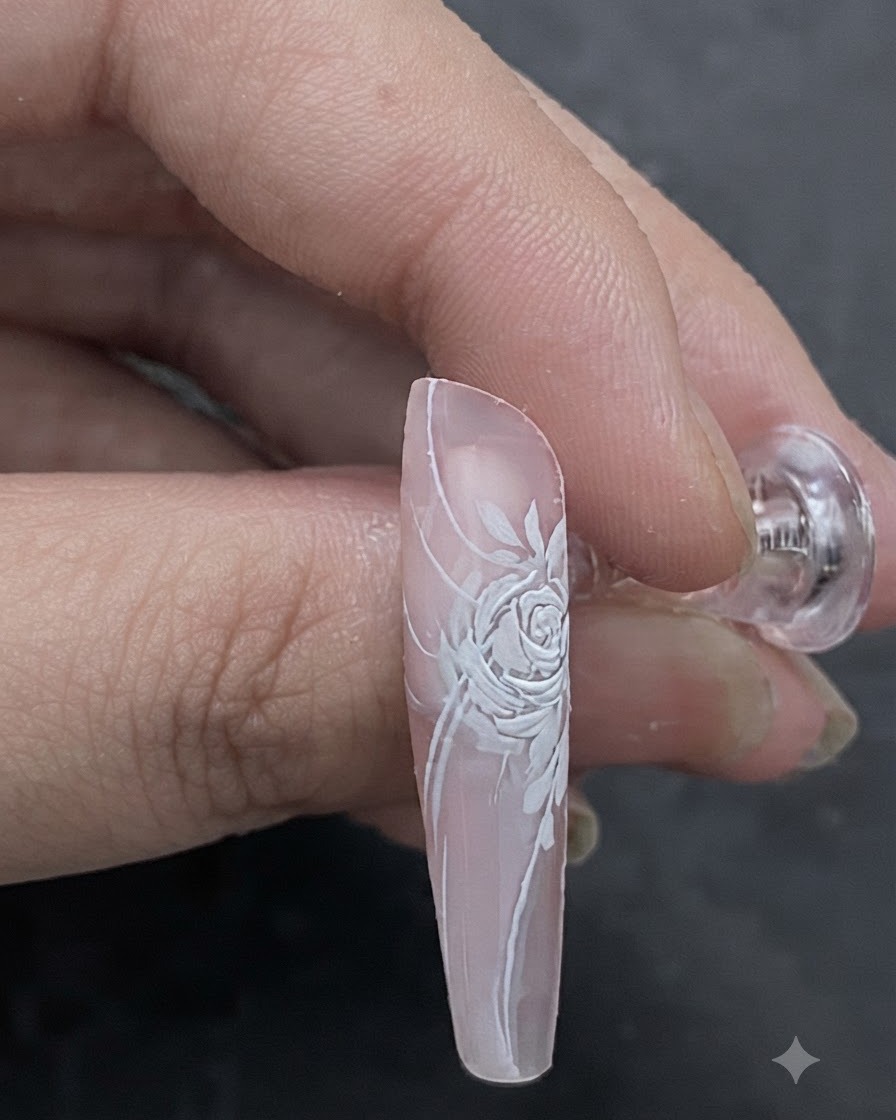 A close-up image showing a light pink shade being brushed onto the center of a dimensional white rose nail design.