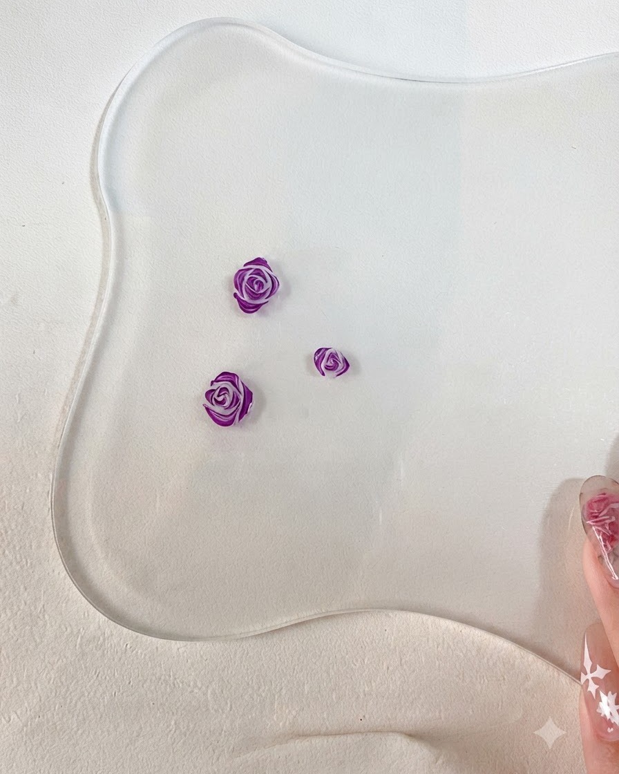 A close-up of a fine nail art brush adding detailed dark purple outlines to the edges of sculpted 3D rose petals.