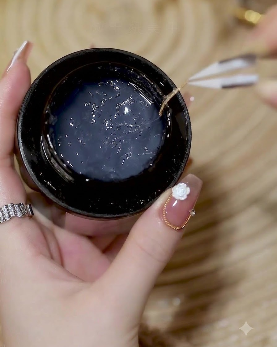 Tweezers holding a delicate gold chain over a jar of builder gel.