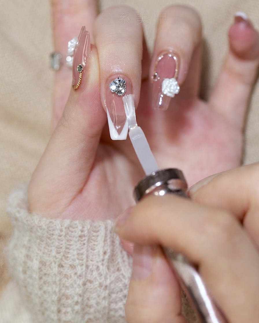 A nail brush applying a shiny top coat onto a French tip nail while avoiding the rhinestone cluster.