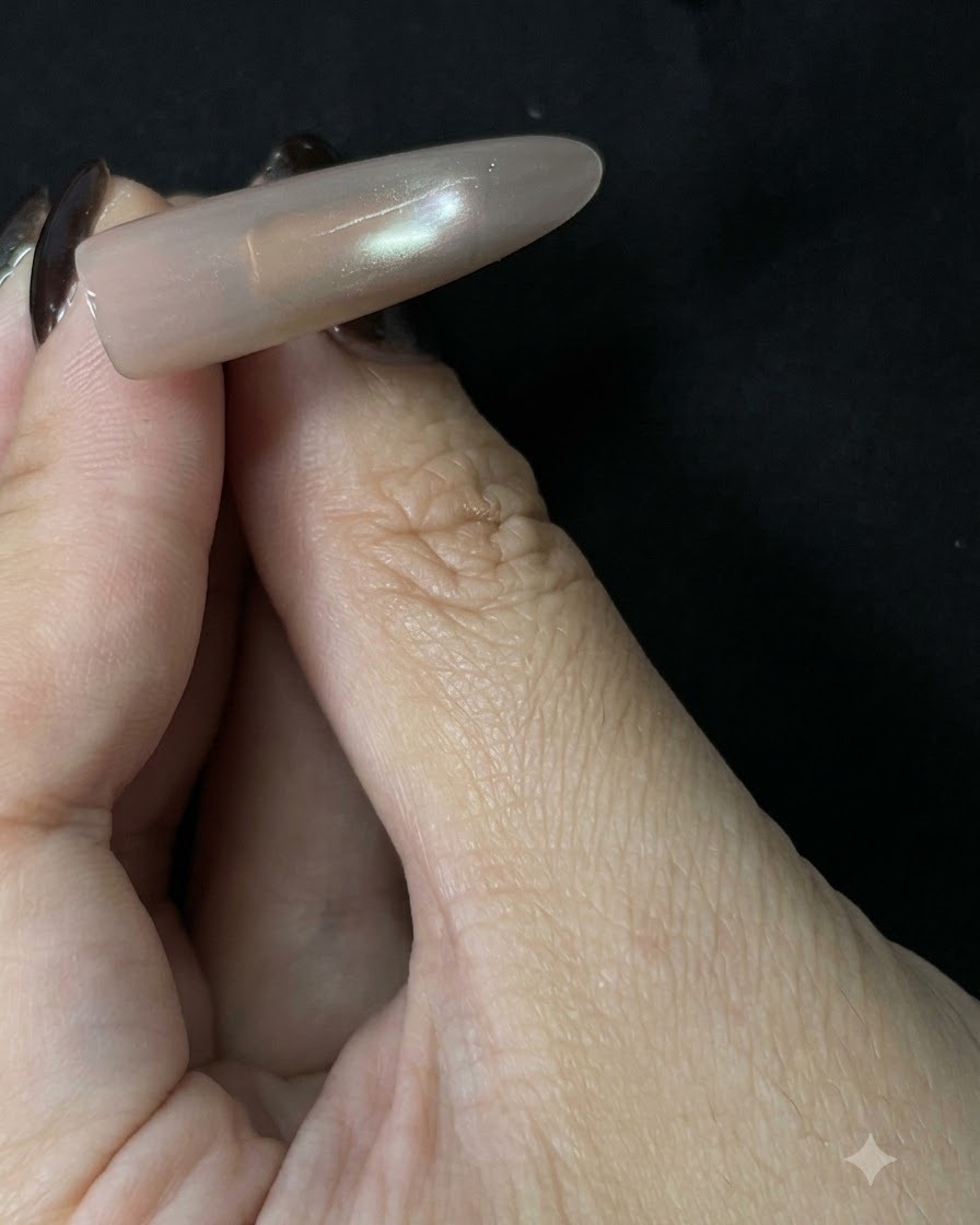 A finished long nude cat-eye nail extension held up against a dark background, showing a soft reflective center line.