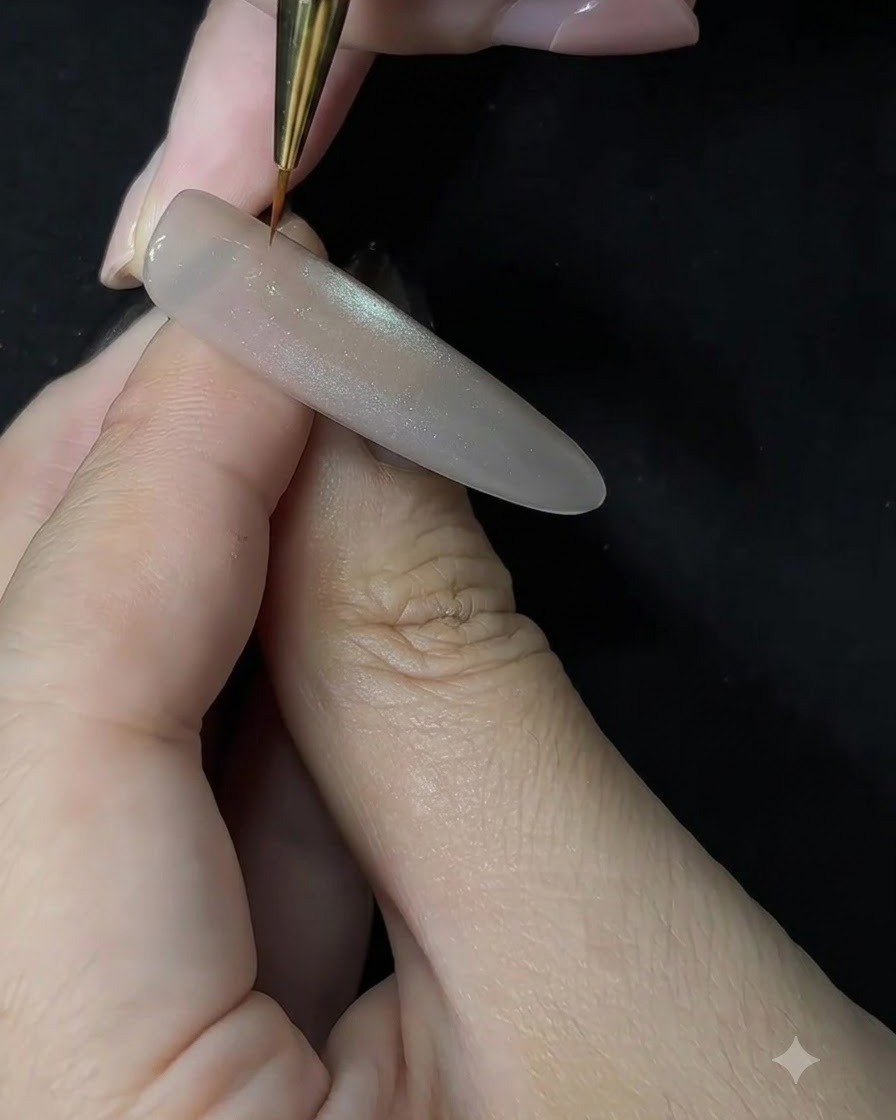 A close-up of a nail artist using a fine detail brush to apply white gel in a dabbing motion onto a sculpted nail extension.