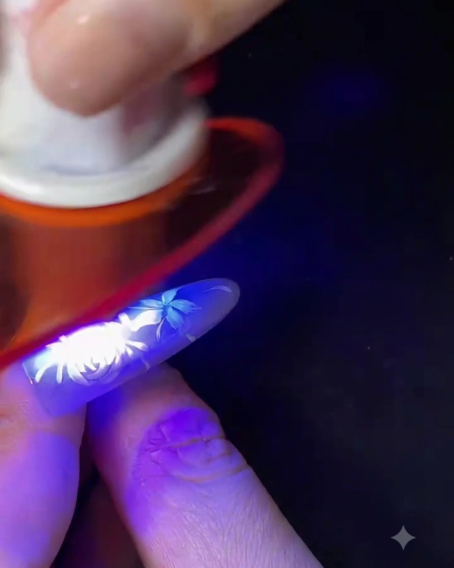 A finger with completed white floral nail art curing under a small blue UV/LED nail lamp.