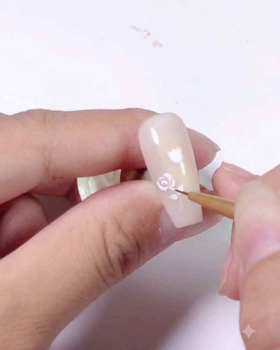 A completed white rose design painted on the upper section of a light pink nail.
