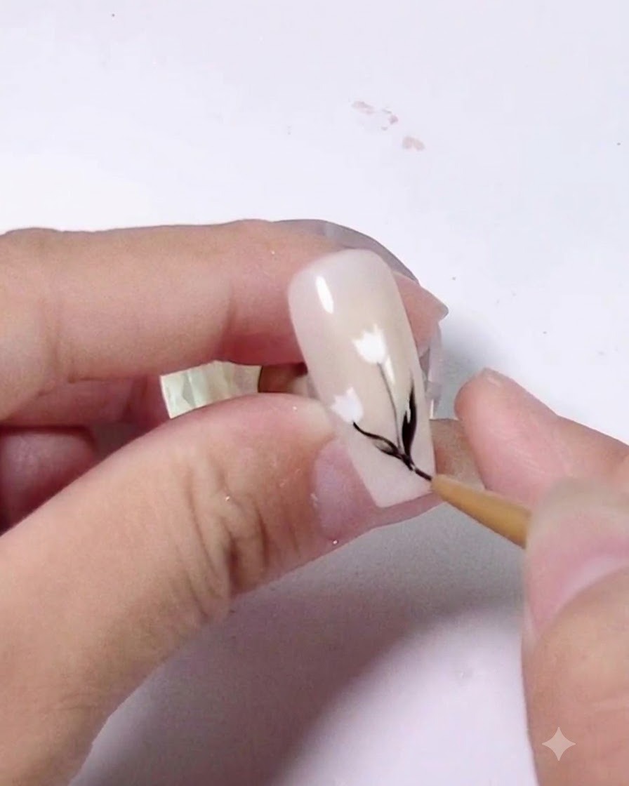 A close-up showing small black leaf details being added along the stem on a decorated nail.