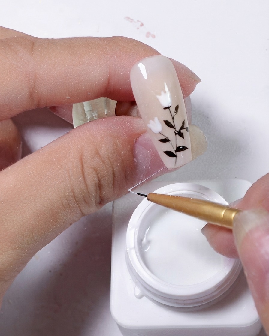 A nail being decorated as an elastic string of white gel is draped diagonally across the surface.