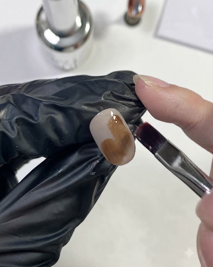 A nail brush applying light caramel brown gel in a large patch on the nail.