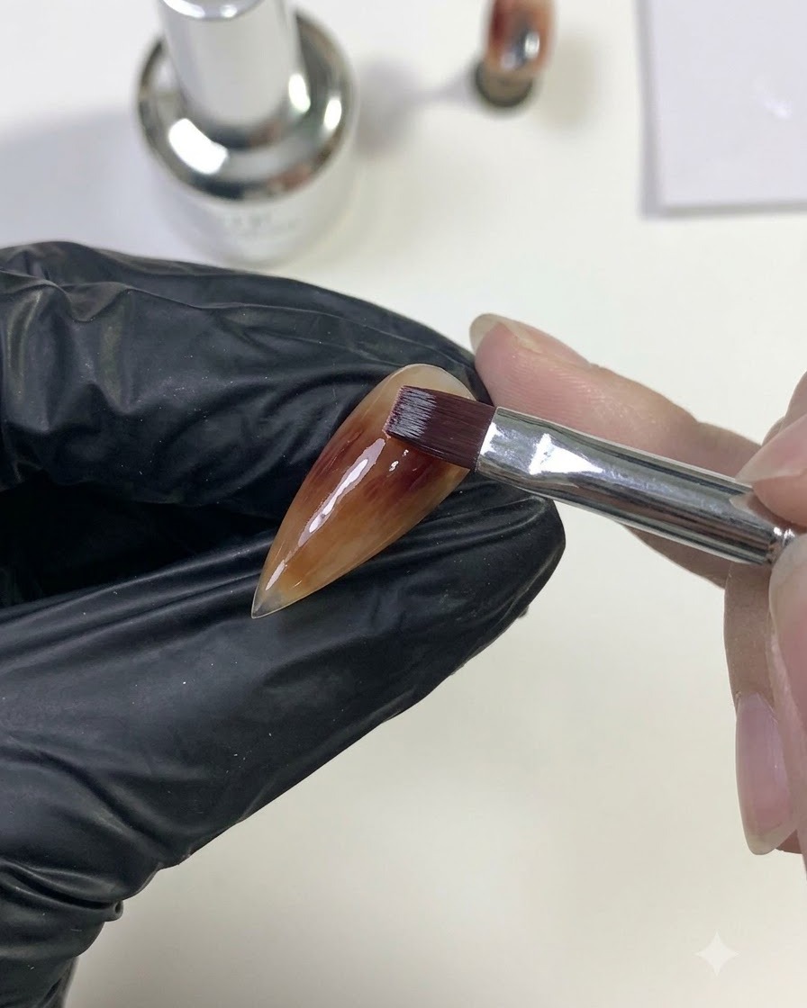 A brush blending deep red gel outwards to merge with the caramel base layer.