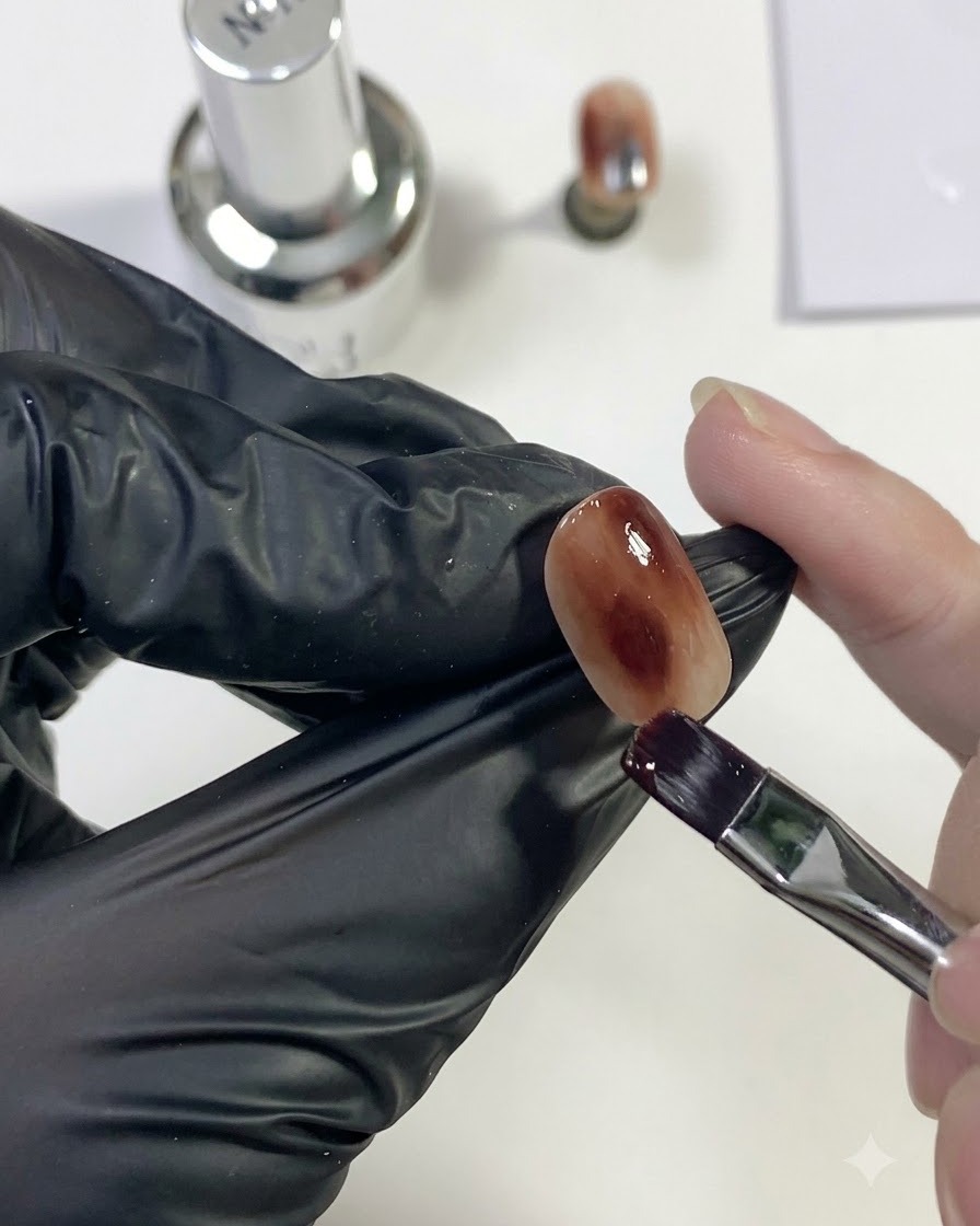 A detailed close-up showing a brush softly feathering and blending dark brown gel into the amber background.