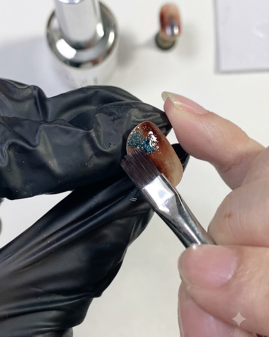 A nail brush placing a small dab of sparkly blue magnetic cat-eye gel onto the side of the amber nail.