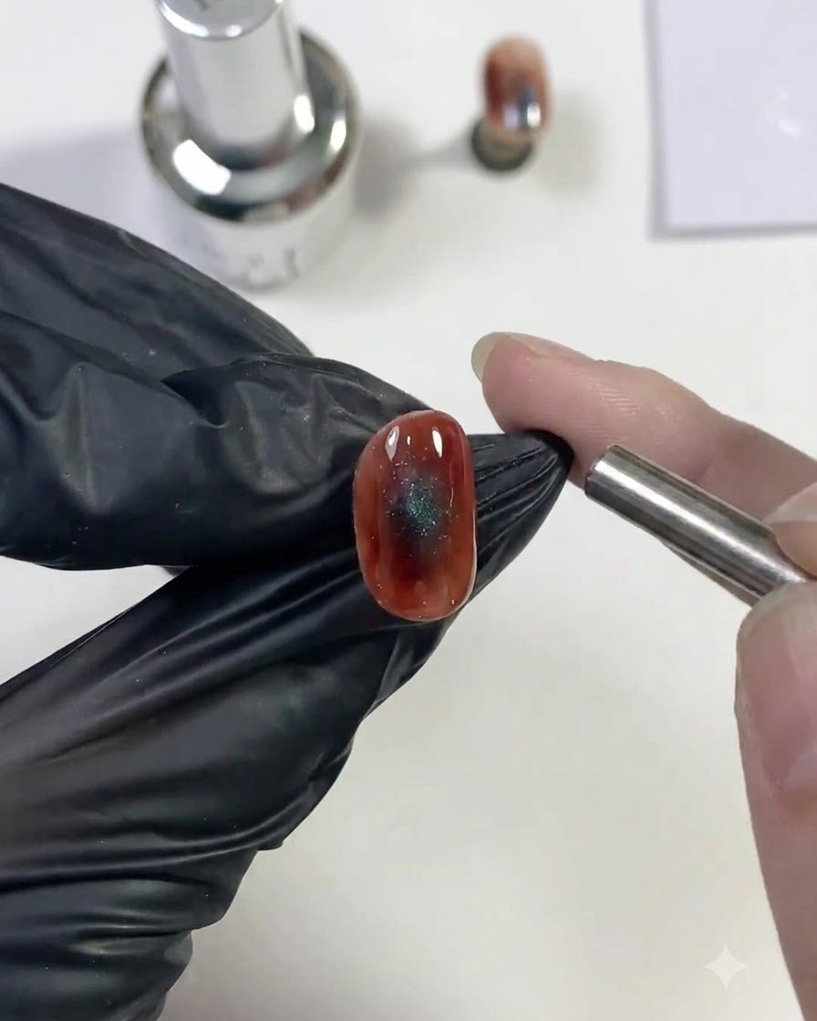A cylindrical magnet held close to a wet blue cat-eye nail design to pull the sparkling light reflection.
