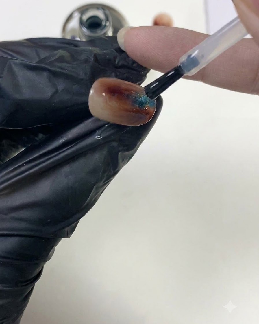 A nail brush smoothing clear top coat over a textured amber nail surface to build the apex.