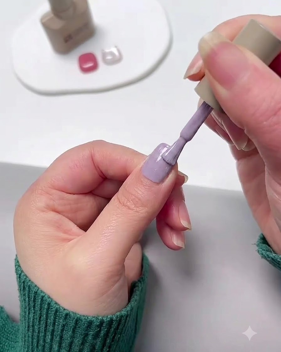 A nail brush applying lavender purple gel polish onto a fingernail.