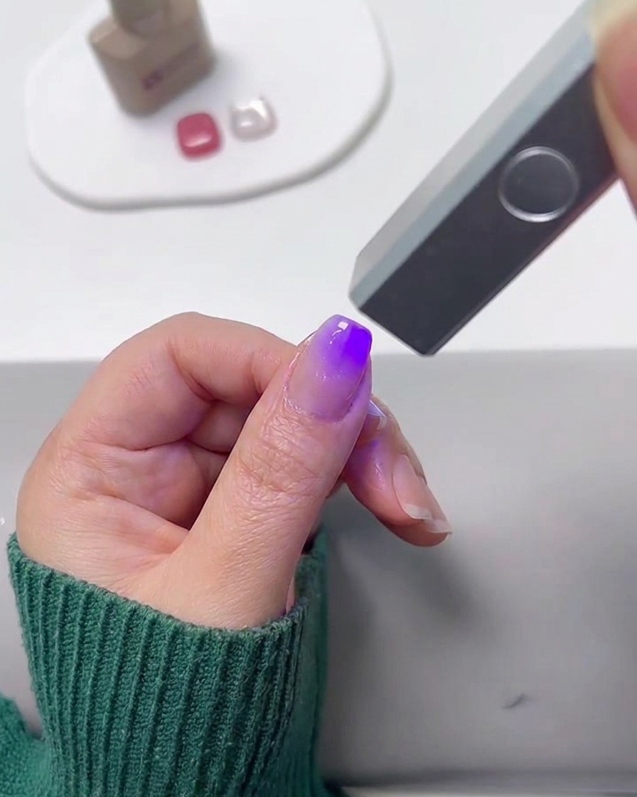 A mini UV lamp curing a gradient-painted fingernail.