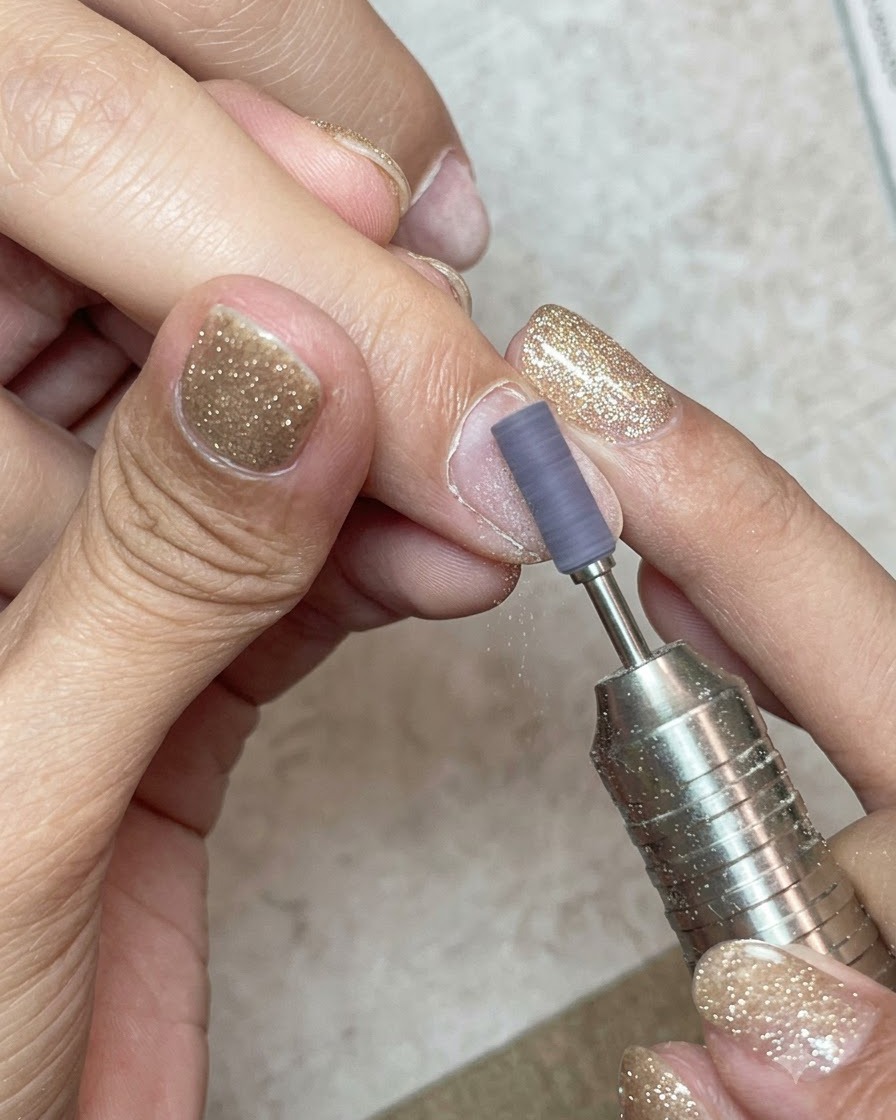 A sanding band on an e-file gently buffing the surface of a natural nail plate.