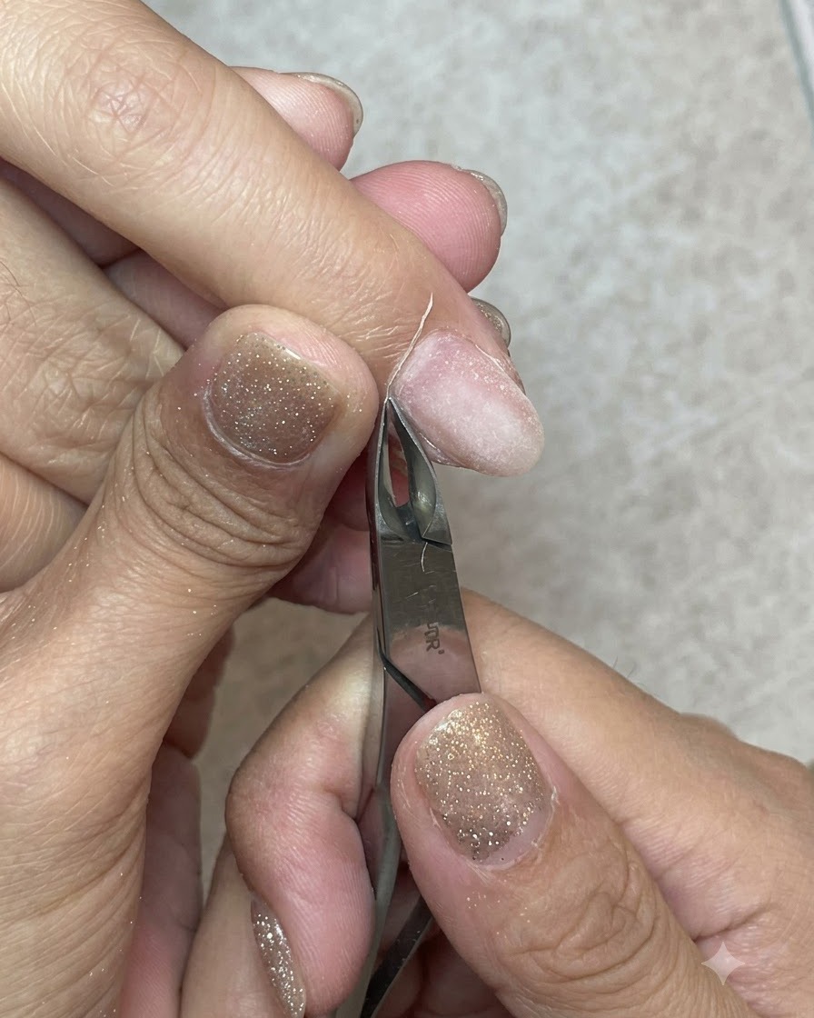 Sharp metal cuticle nippers cleanly trimming away a strip of dead skin from the cuticle line.