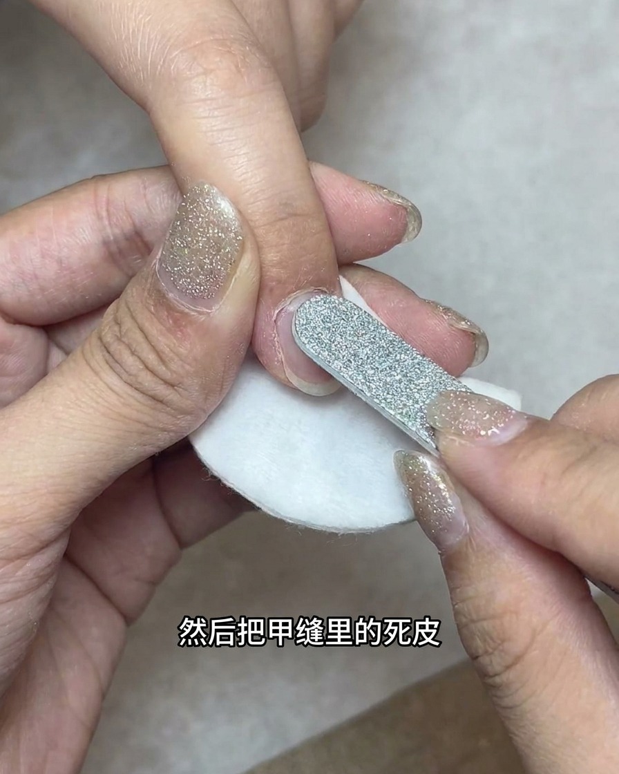 An e-file with a bullet-shaped bit cleaning the lateral nail folds over a cotton pad.