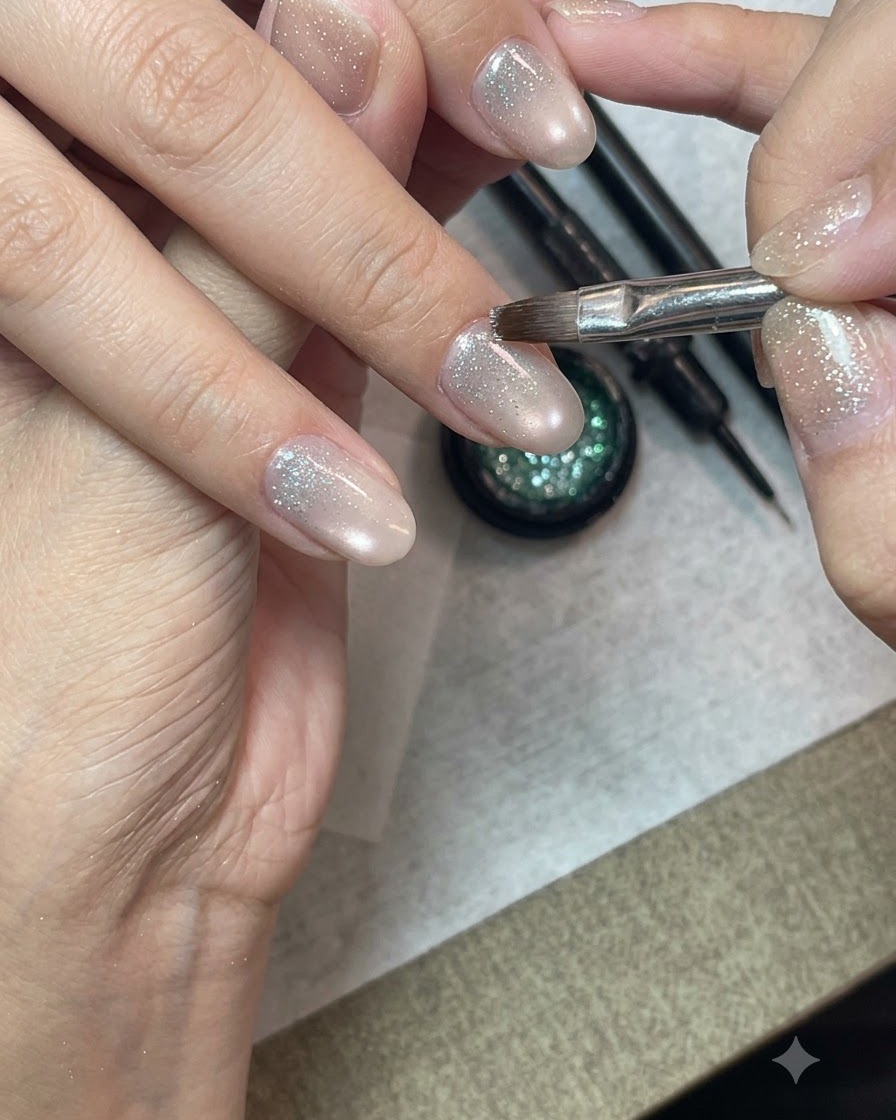 A detailed nail art brush applying crushed diamond glitter gel onto the lower half of a prepped fingernail.