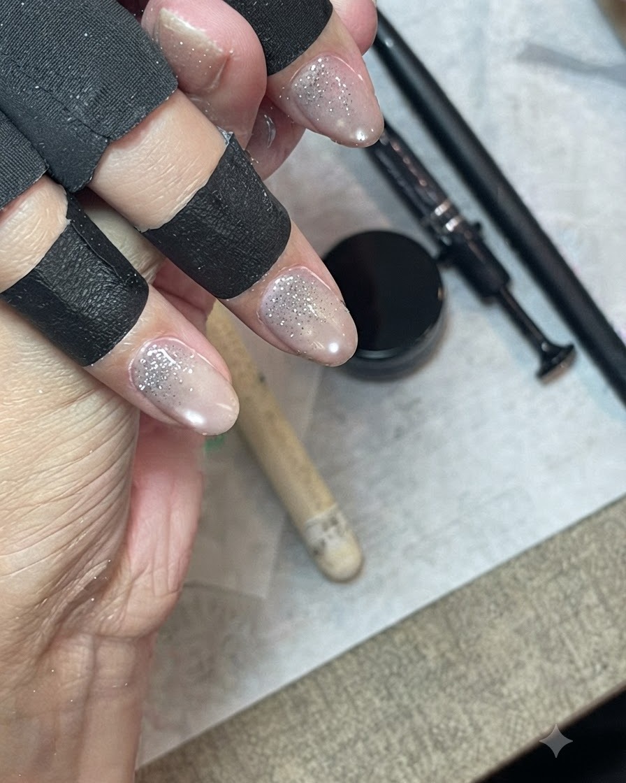 A hand wearing black finger protectors using a fine liner brush to feather and blend glitter gel down the nail.