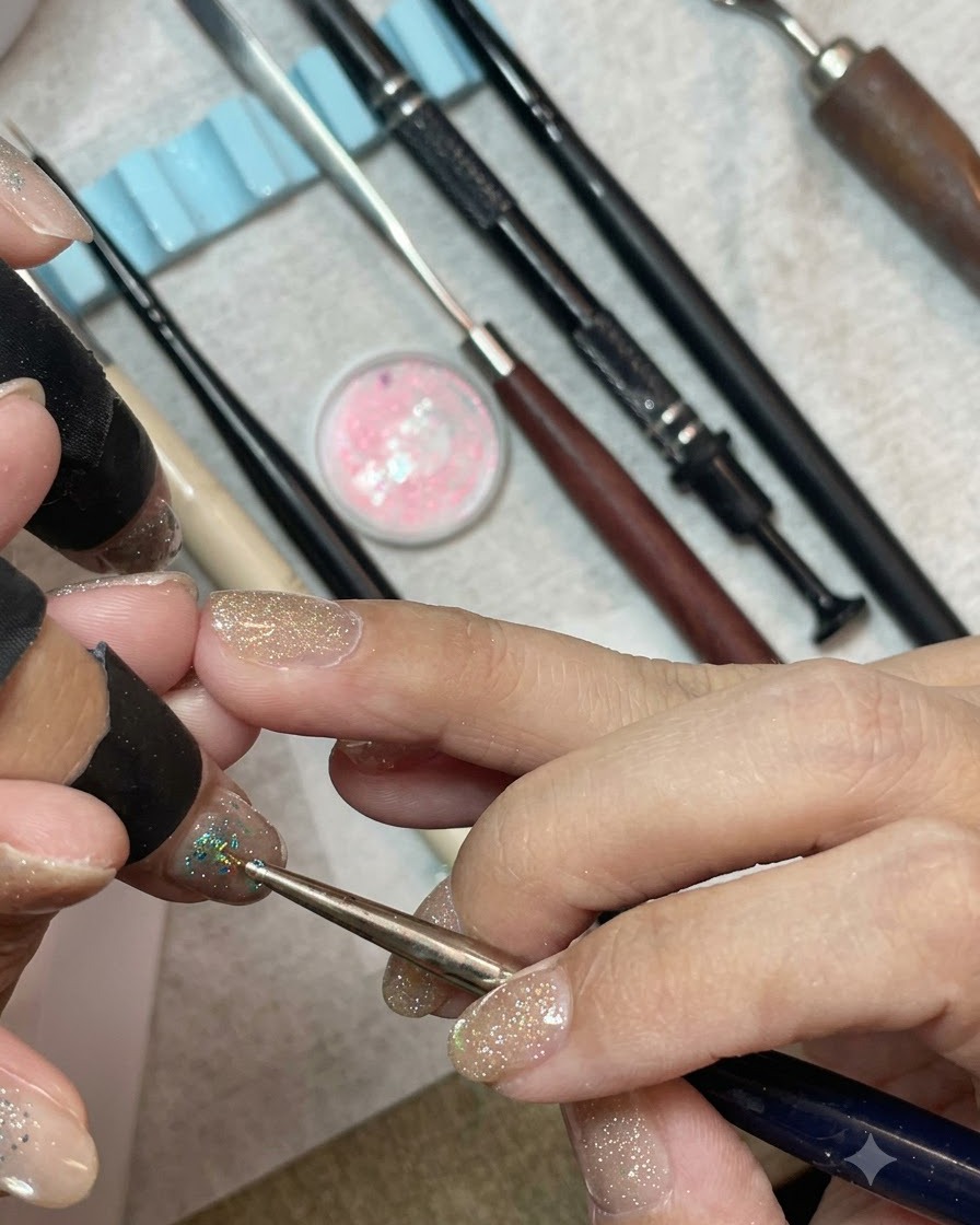 A detail brush placing chunky mint blue and silver hexagonal sequins densely onto the tip of a gel-polished nail.