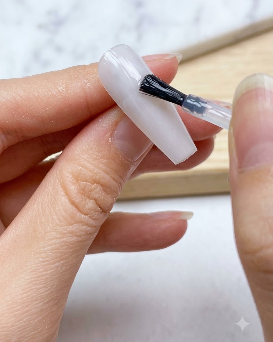 A nail brush applying a smooth layer of translucent milky white gel base over the entire nail.