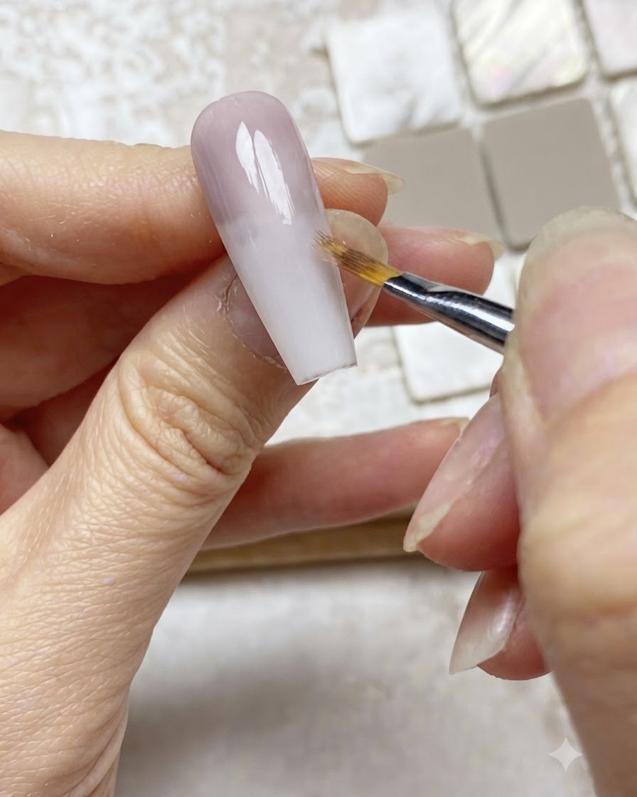 An ombre brush softly feathering the edge of a purple gel layer downward on a nude nail extension.