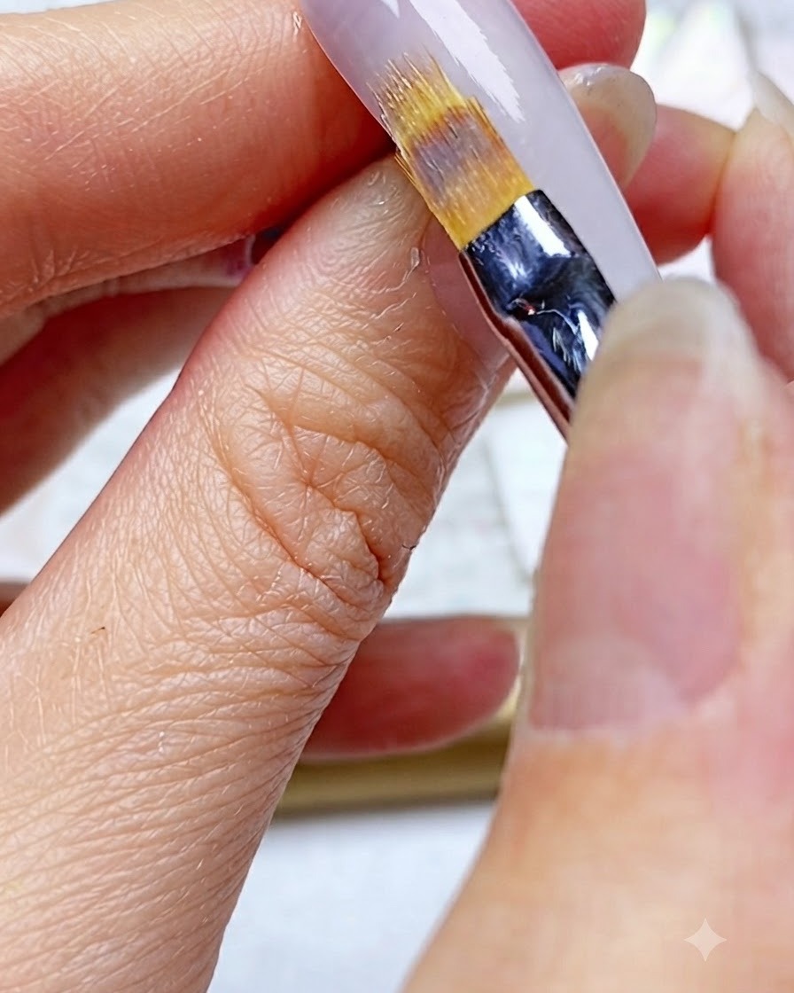 An ombre brush being wiped clean on a white cleansing pad.