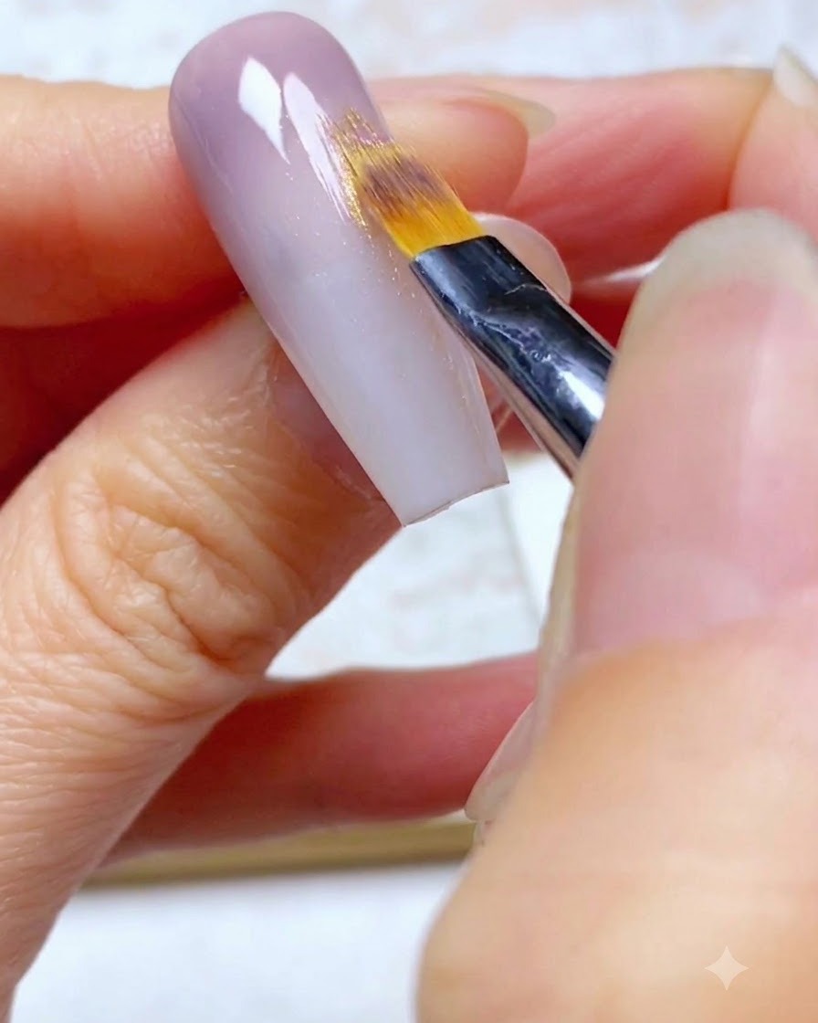 An ombre brush feathering the second layer of purple gel downwards onto the nail.