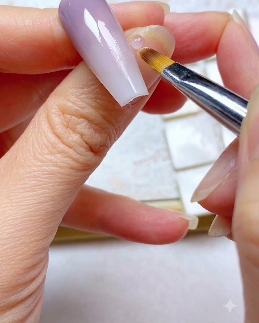 A close-up of an ombre brush lightly sweeping the upper purple section of a gradient nail.