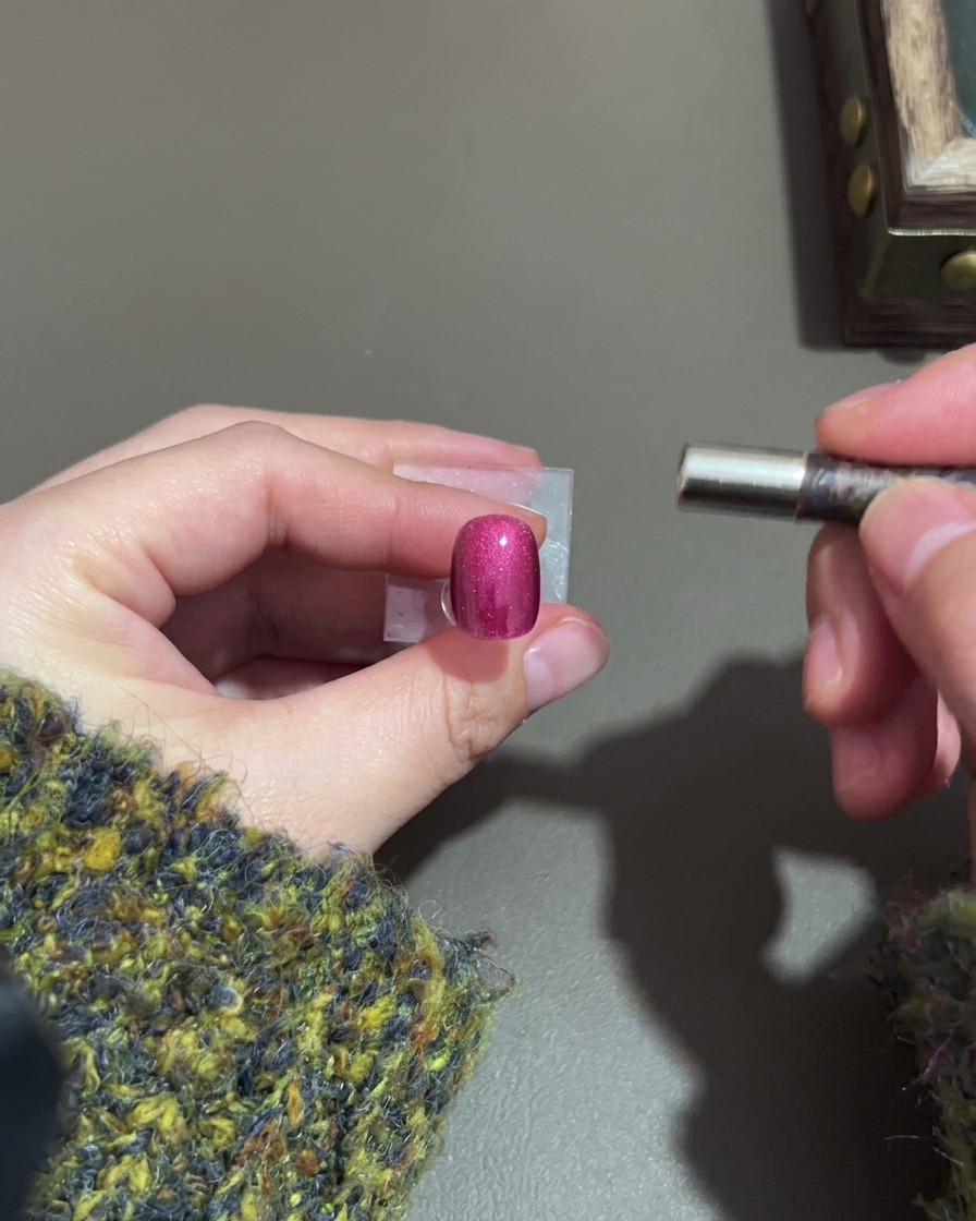 A hand holding a magnet beside a dark purple cat-eye nail to form a highlight.