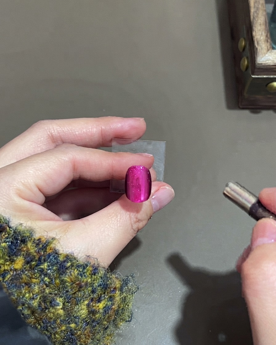 A small cylindrical magnet hovering near a pink cat-eye gel nail to shape the highlight.
