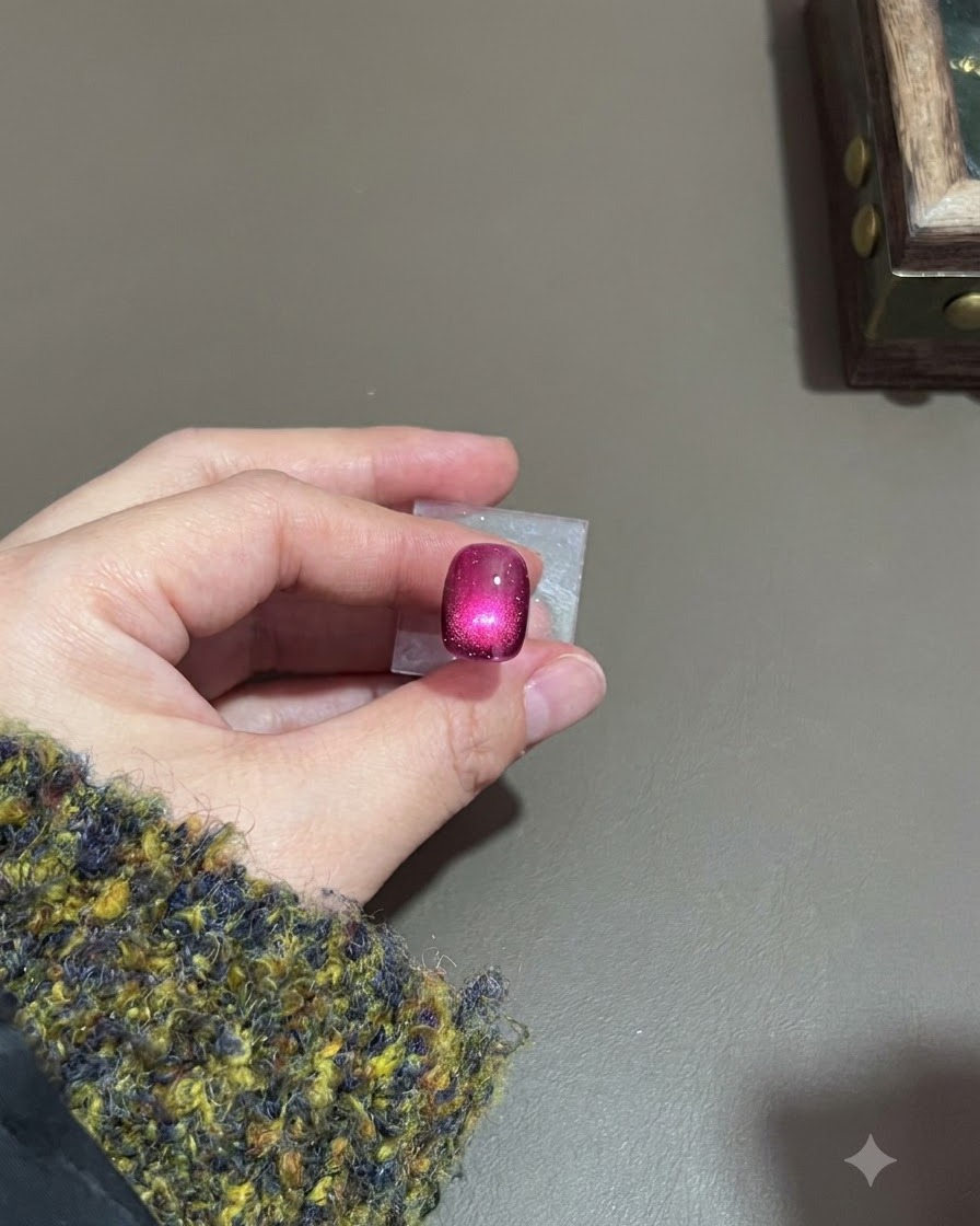 A dark purple cat-eye nail with a cured glowing highlight under a lamp.