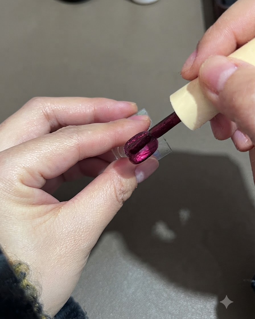A brush smoothing out a second layer of purple cat-eye gel polish on a nail display stand.