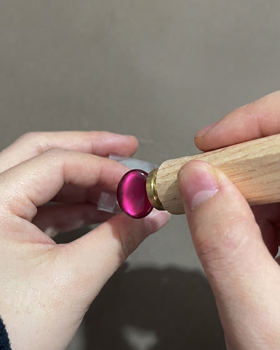 A hand holding a nail stamp tool near a finished purple gradient cat-eye nail.