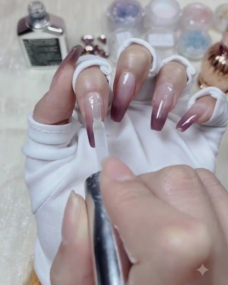 A bottle brush applying clear leveling gel across the entire surface of a gradient-painted nail.
