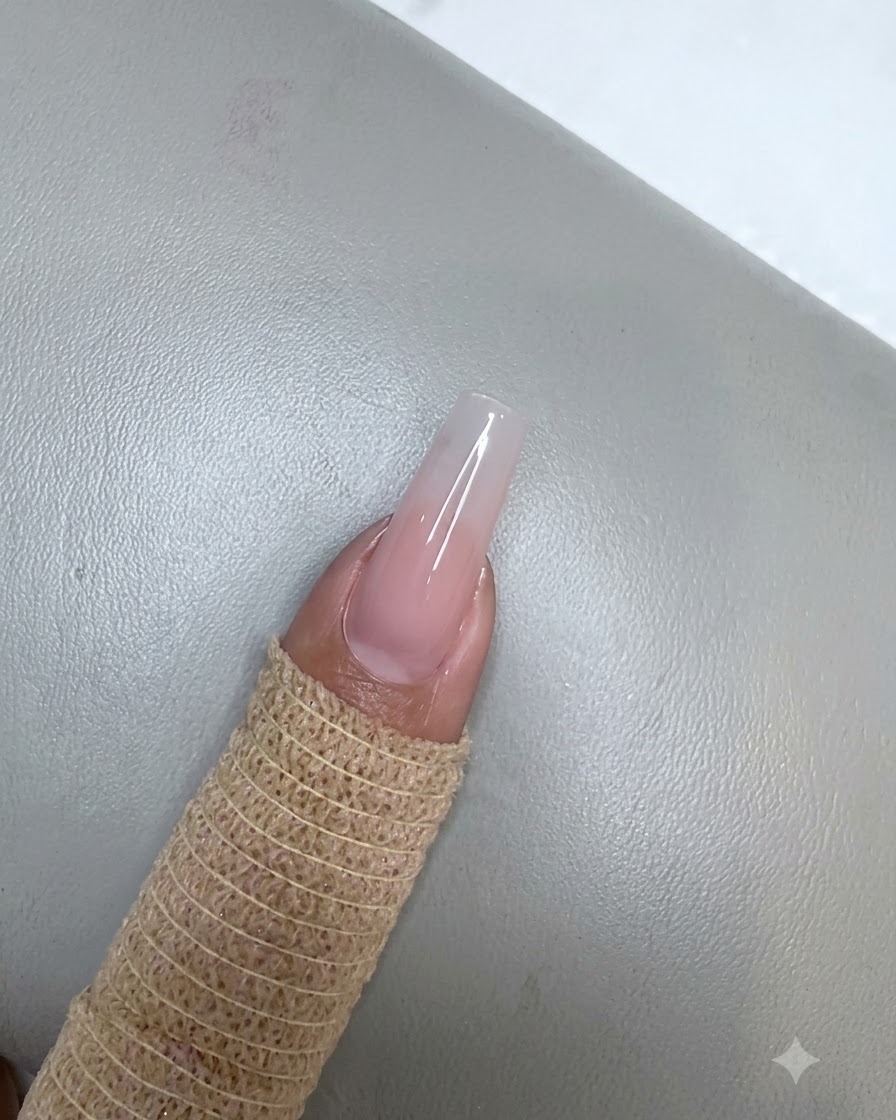 A fingernail with a cured nude pink gel application resting underneath a small purple UV LED lamp.