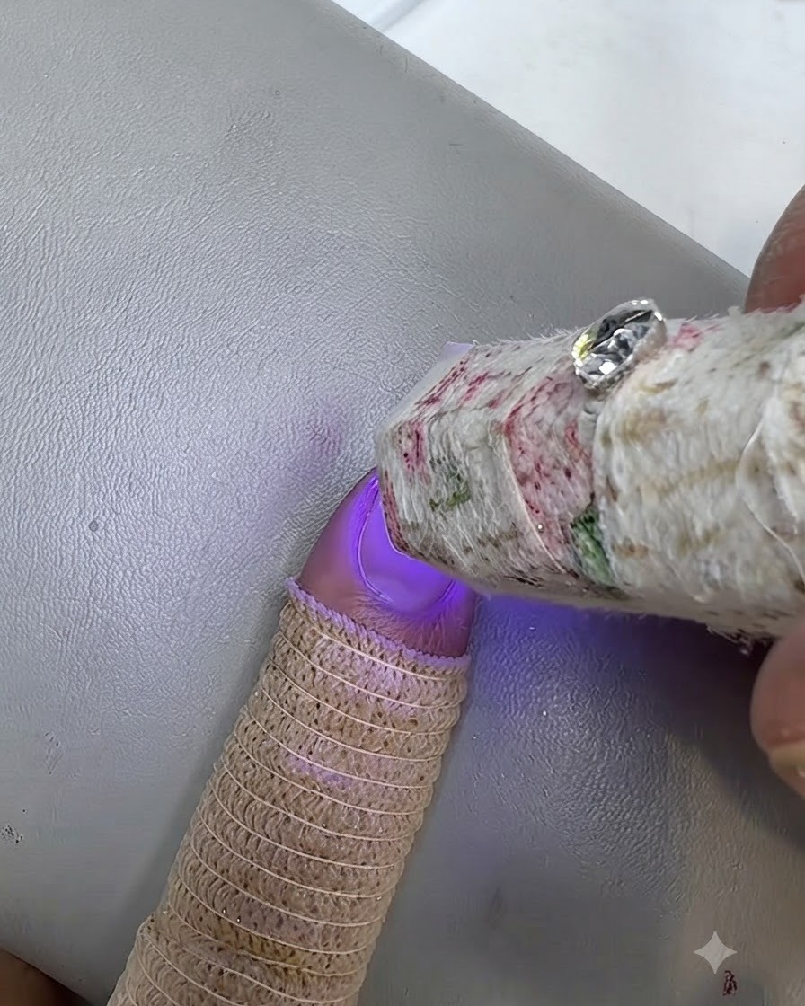 A small UV lamp curing a painted nail with a finger wearing a knitted finger guard.