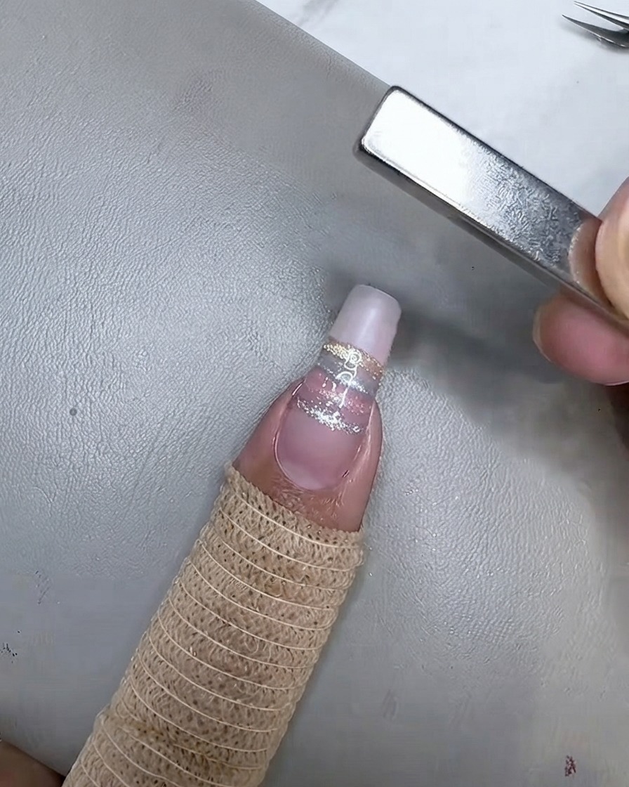 The nail curing under a mini UV/LED lamp after the champagne cat eye stripe has been magnetized.