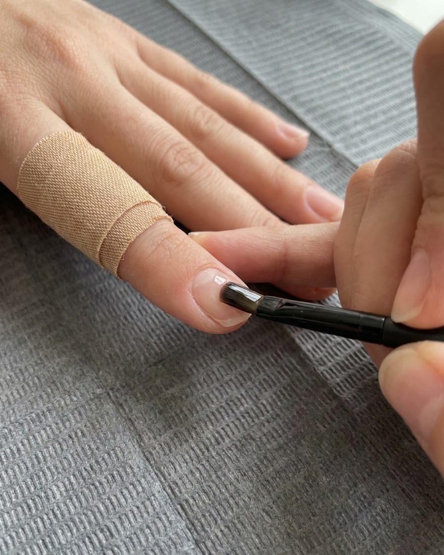 A flat gel brush applying a clear layer of reinforcement gel over the decorated nail.