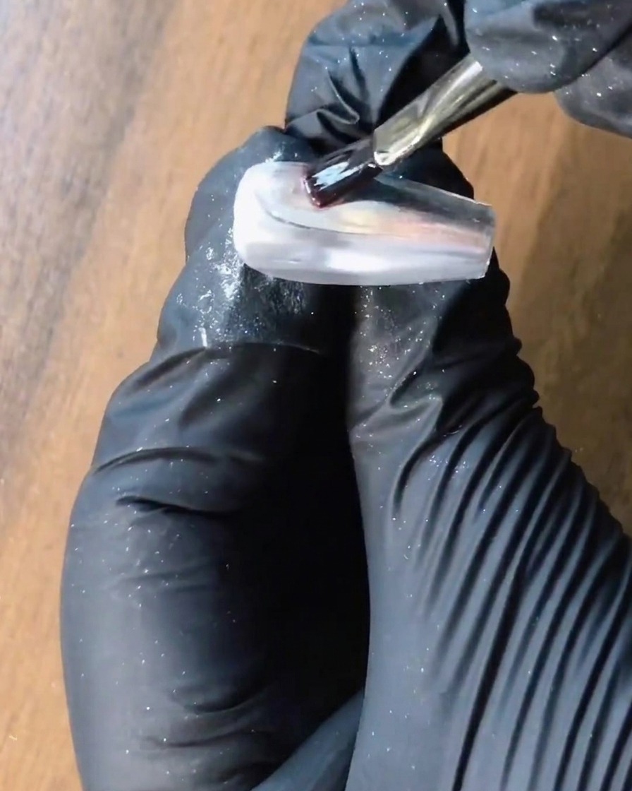 A brush applying clear reinforcement gel over a silver chrome nail.
