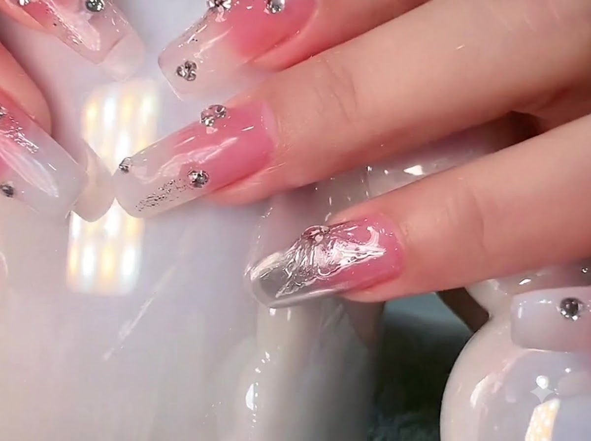 Close-up of long square nails with milky white gradient and rhinestones being held against a white ceramic mug.