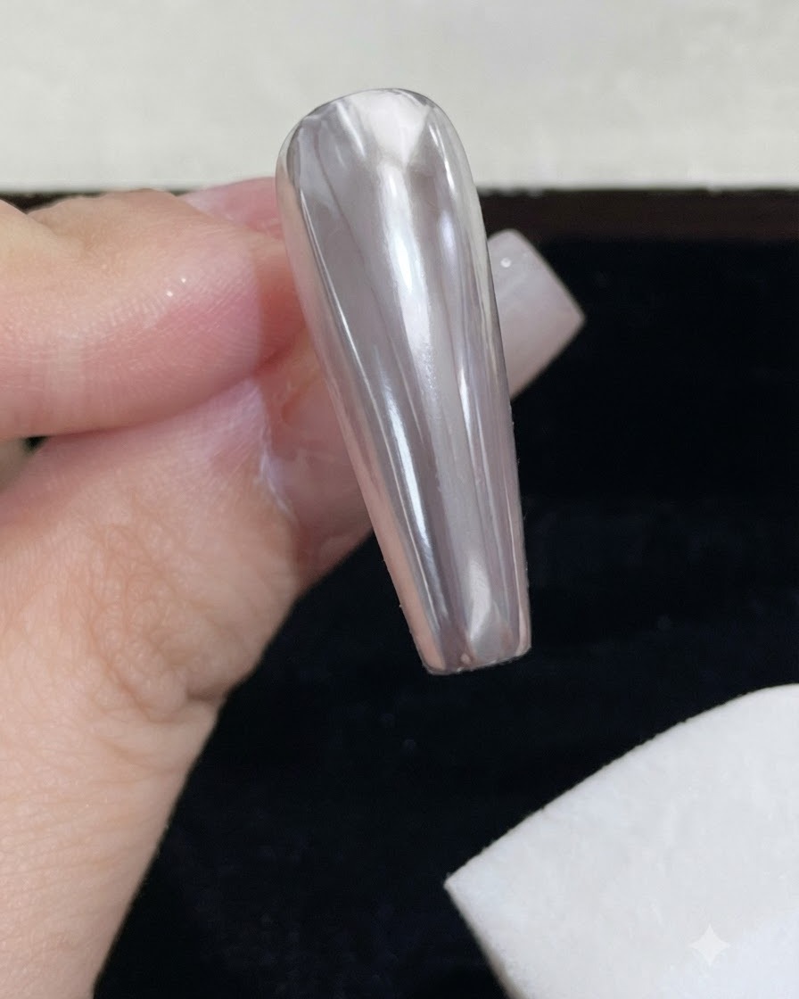 A white foam sponge block wiping excess mirror powder off a glossy chrome nail.