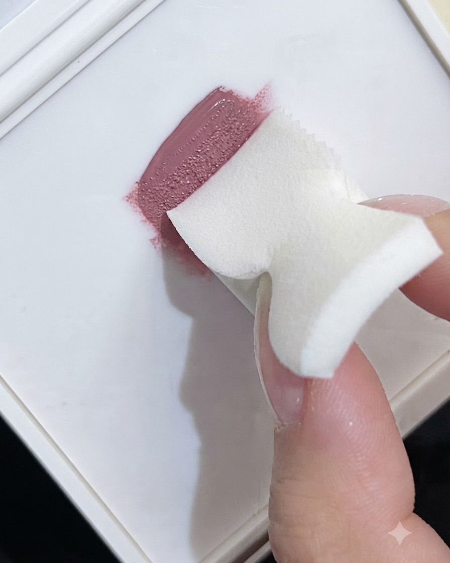 A foam makeup sponge picking up pink gel polish from a white palette to create a gradient texture.