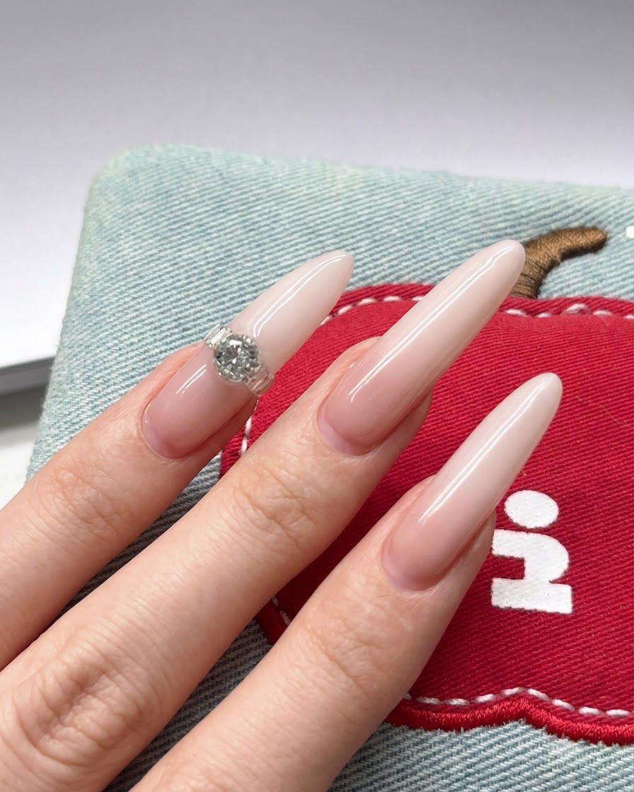 A close-up of a nail brush applying white gel pigment to the tip of a long nude stiletto nail.