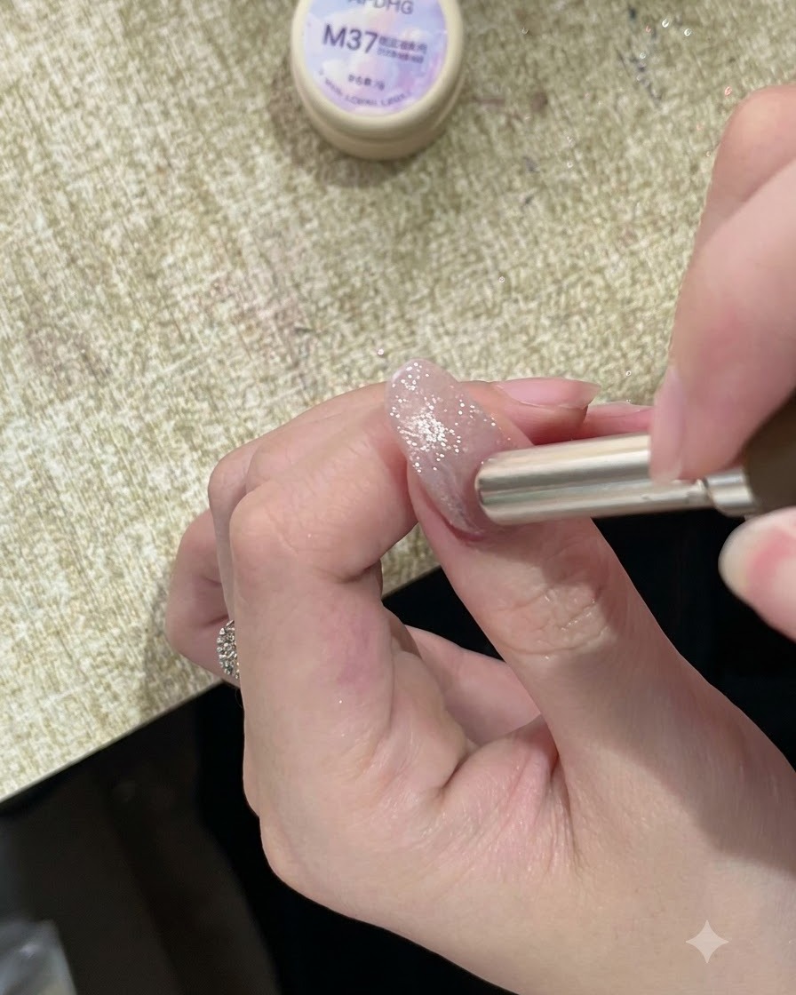 A cylindrical magnet held near the cuticle of a sparkly painted nail, directing the magnetic shimmer upward.