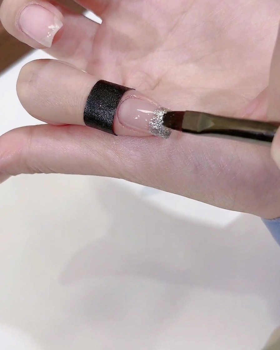 A brush applying a dab of clear diamond glue onto a decorated nail tip.