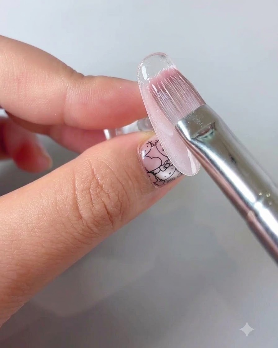 A manicure brush applying a clear sealing top coat over a floral nail design.