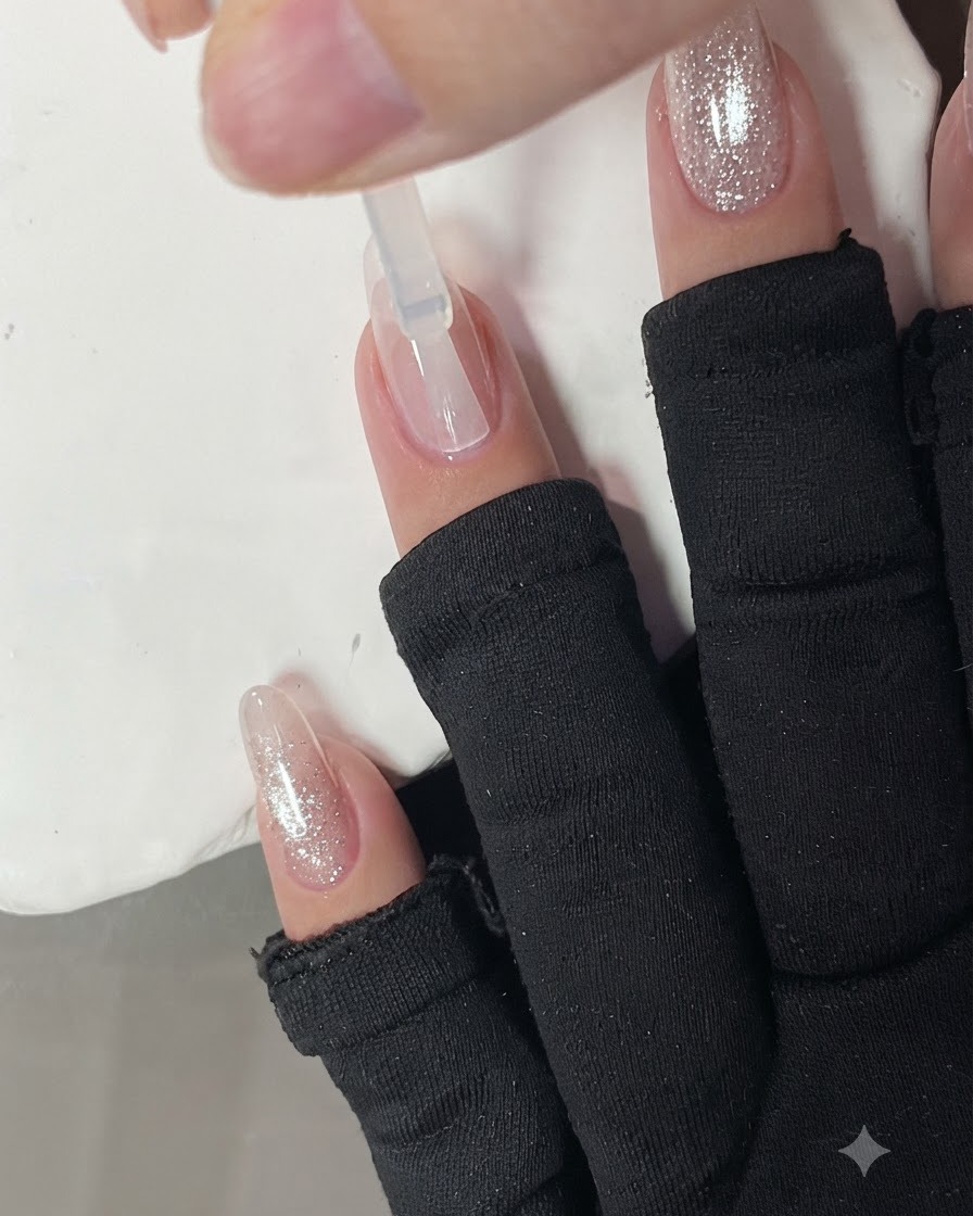 A clear base coat being applied to a nail with a brush.